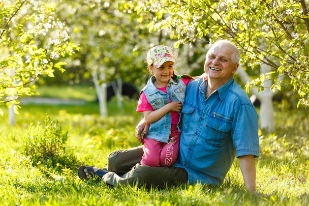 Grootvader met kleindochter rusten in lentetuin - Foto, afbeelding