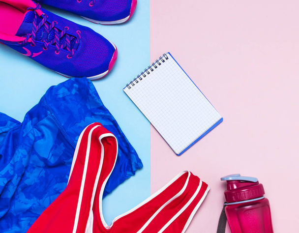 Ультрафіолетові жіночі кросівки, рожеві верхні сині спортивні легінси та пляшка води на пастельному рожевому фоні плоский вигляд зверху з копіювальним простором. Спортивне взуття, фітнес концепція здорового способу життя
. - Фото, зображення