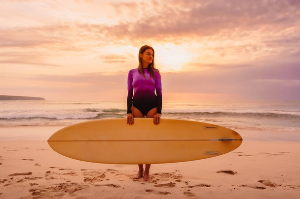 Surf dziewczyna z deski surfingowej pobyt na plaży na zachód lub wschód słońca. - Zdjęcie, obraz