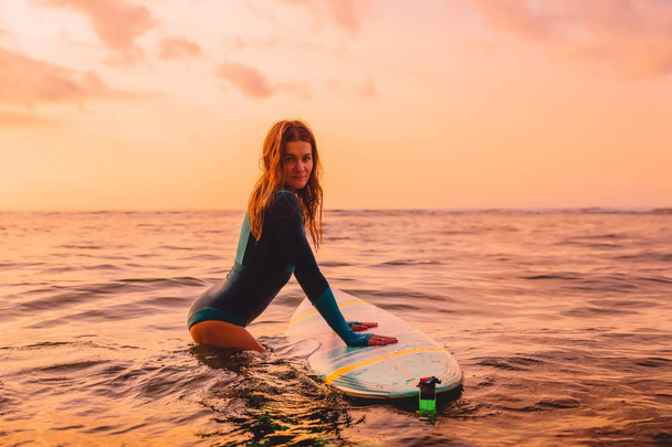 Attrayant surfeur femme posant avec planche de surf dans l'océan. Surfer au coucher du soleil
 - Photo, image