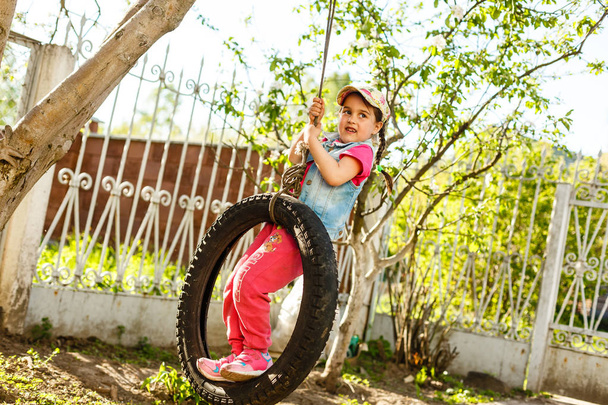Szczęśliwy mała dziewczynka swinging na huśtawce opony w zielonym ogrodzie  - Zdjęcie, obraz