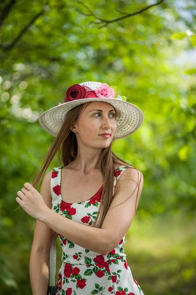 Portret van een mooie elegante vrouw in lichte witte jurk en muts permanent in het park van de zomer. - Foto, afbeelding