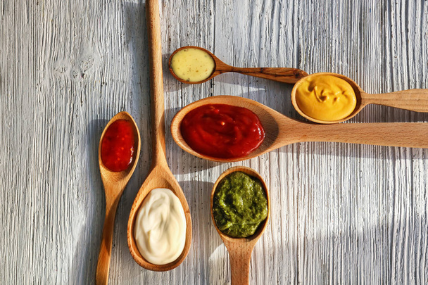 Cucharas con sabrosas salsas sobre mesa de madera blanca
 - Foto, imagen
