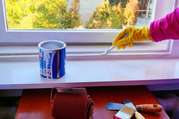 La mano in guanti di gomma gialli applica una finitura di vernice bianca lucida a una struttura di finestra
. - Foto, immagini