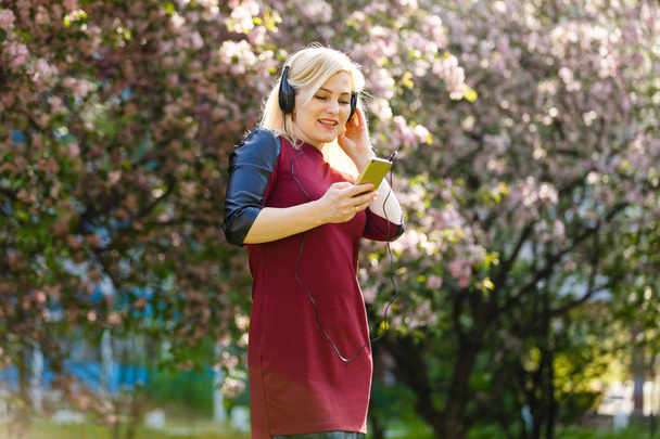 Portrait of young woman with headphones listening music in spring park - Fotoğraf, Görsel
