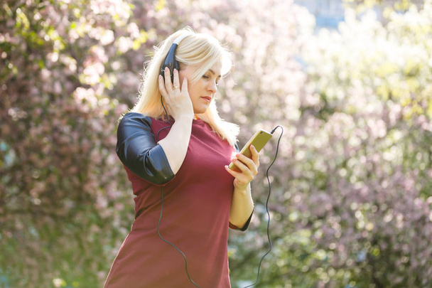 fiatal nő a fejhallgatóban zenét hallgat a virágzó parkban - Fotó, kép