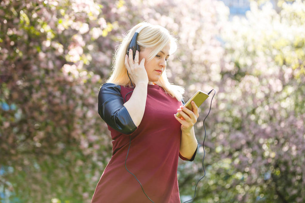 Nuori nainen kuulokkeissa kuuntelemassa musiikkia kukkivassa puistossa
 - Valokuva, kuva