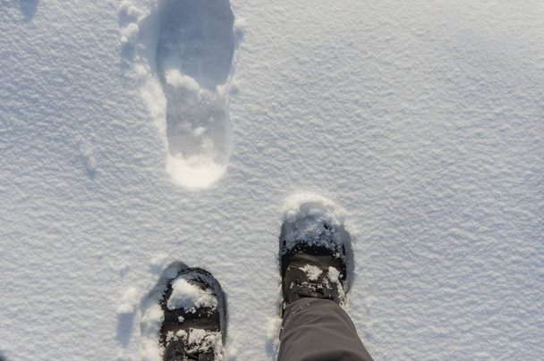 Paisaje de invierno con piernas humanas que usan botas y dan pasos sobre una nieve fresca
 - Foto, imagen