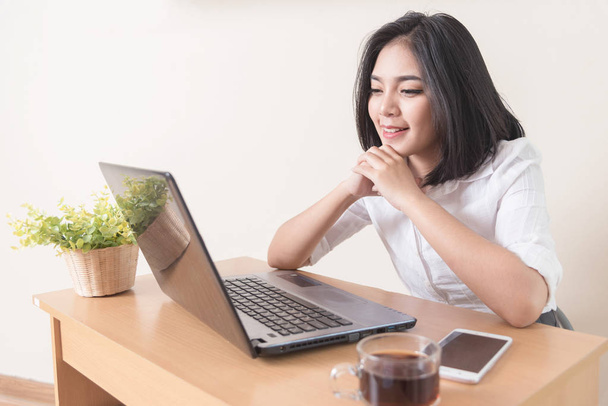 Portrét šťastný úspěšná podnikatelka Kavkazský v bílé košili dívá a usmívá se na kameru notebooku. Atraktivní žena manažer sedí u stolu po náročném pracovním dni. - Fotografie, Obrázek