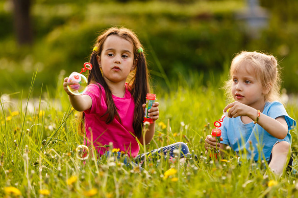 Malé dívky při západu slunce foukající v zeleném parku mýdlové bubliny - Fotografie, Obrázek