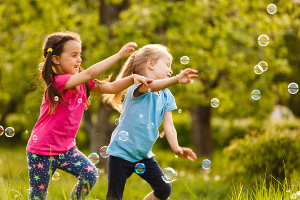 Dos chicas felices por las burbujas de jabón flotantes en el parque verde al atardecer
 - Foto, Imagen