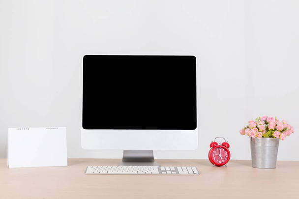 Ordenador personal moderno con pantalla de espacio de copia en blanco en el escritorio con teclado, flor en maceta, reloj rojo y calendario. Maquillaje del lugar de trabajo
. - Foto, Imagen