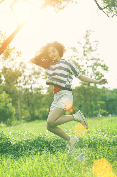 Happy young woman jumping in park with sunlight. Freedom lifestyle. Vacation and travel concept. - Photo, image