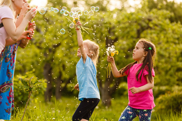 Kaksi tyttöä leikkii vihreässä puistossa ja puhaltaa kelluva saippuakuplia
 - Valokuva, kuva