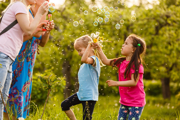 Mães com filhas soprando bolhas de sabão no parque verde
 - Foto, Imagem