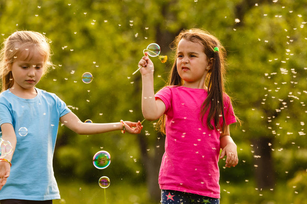 Dos chicas jugando en el parque verde y soplando burbujas de jabón flotante
 - Foto, Imagen