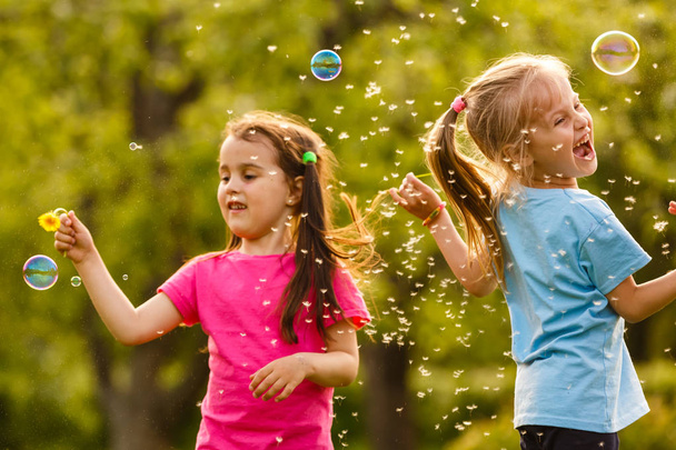 Two girls playing in green park and blowing floating soap bubbles - Photo, Image