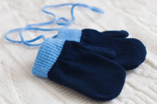 Pair of blue knitted mittens on a white woolen fabric. Winter background. - Fotó, kép