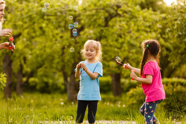Twee meisjes spelen in groen park en zwevende zeepbellen blazen - Foto, afbeelding