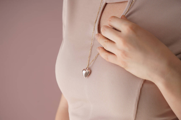Woman wearing heart-shaped pendant on color background, closeup - Foto, afbeelding