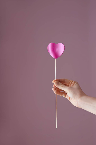 Woman holding stick with paper heart on color background - 写真・画像