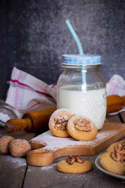 gingerbread cookies with walnuts on a table and a cup of mil - Фото, изображение