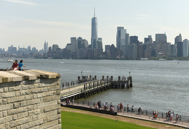 New York, USA - June 09, 2018: Tourists near the Statue of Liberty and the Lower Manhattan skyscrapers at the background. - Photo, image