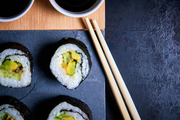 Vegane Sushi-Rollen mit Nori-Algen, Sushi-Reis, Gurken und Avocado. Ansicht von oben mit Kopierraum - Foto, Bild