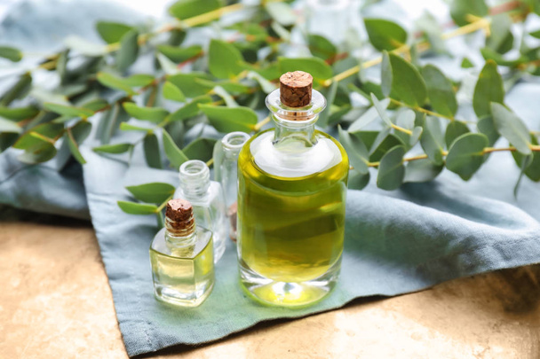 Bottles with essential oil and eucalyptus branches on table - Foto, Bild