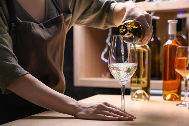 女性のバーテンダーがカウンターにグラスにボトルからワインを注ぐ - 写真・画像