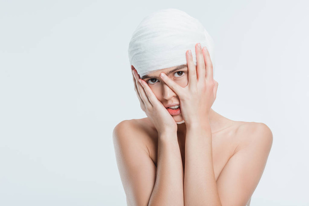 naked woman with white bandages and hands on face isolated on white - Φωτογραφία, εικόνα