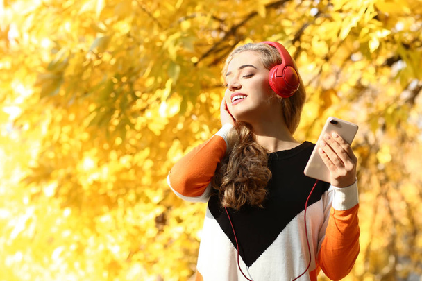 Beautiful young woman listening to music in autumn park - Photo, Image