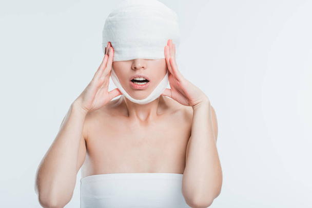 vyděšená žena s bílým obvazy dotýkat hlavy izolované na bílém - Fotografie, Obrázek