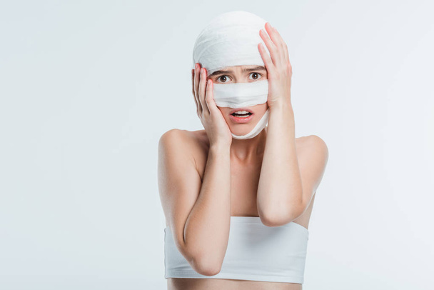 frightened woman with bandages holding head isolated on white - Photo, Image