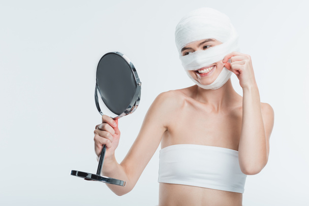 smiling woman with bandages looking at mirror isolated on white - Foto, imagen
