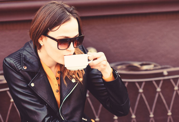Girl in sunglasses drinks tasty coffee on brown terrace background - Fotó, kép