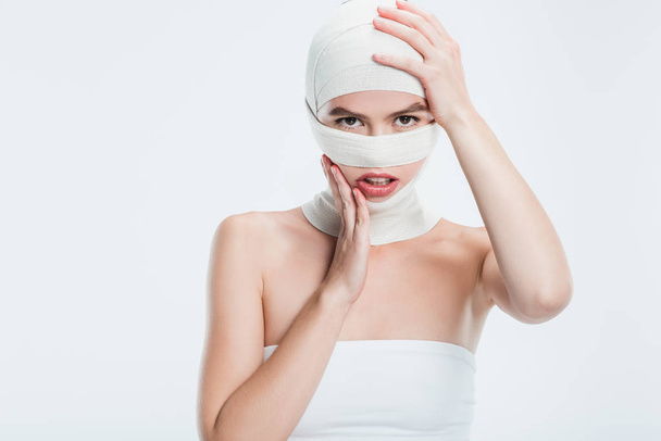 woman with bandages after plastic surgery touching head isolated on white - Foto, Imagen