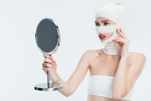 woman with bandages over head looking at mirror isolated on white - Fotografie, Obrázek