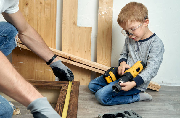Family time: Dad shows his son hand tools, a yellow screwdriver and a hacksaw. They need to drill and drill boards for repair. - Fotoğraf, Görsel