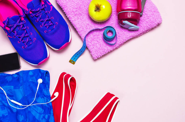 Ультрафиолетовая женская одежда, розовые спортивные ножки и бутылка с водой на розовом фоне - вид сверху с места для копирования. Спортивная обувь, фитнес-концепция здорового образа жизни
. - Фото, изображение