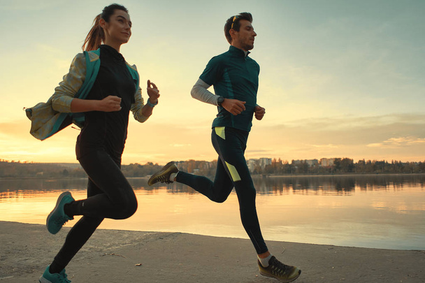 Deux coureurs motivés pour une course sur le lac au lever du soleil. Jeune homme et jeune femme en tenue de sport, courant ensemble. Des personnes sportives s'entraînent à l'extérieur
 - Photo, image