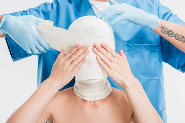 close up of plastic surgeon in gloves taping up woman face with bandage isolated on white - Valokuva, kuva