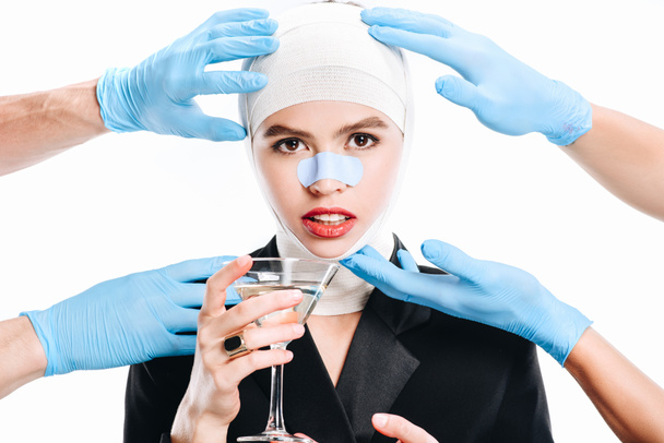 hands in gloves touching woman with bandages after plastic surgery and cocktail isolated on white - Photo, Image