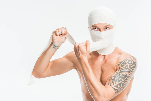 naked man taking off bandages from head after plastic surgery isolated on white - Φωτογραφία, εικόνα