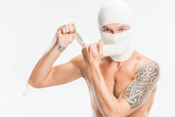 naked man taking off bandages from head after plastic surgery isolated on white - Fotografie, Obrázek