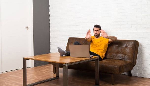 Чоловік з ноутбуком в кімнаті робить стоп жест за розчарований думкою
 - Фото, зображення