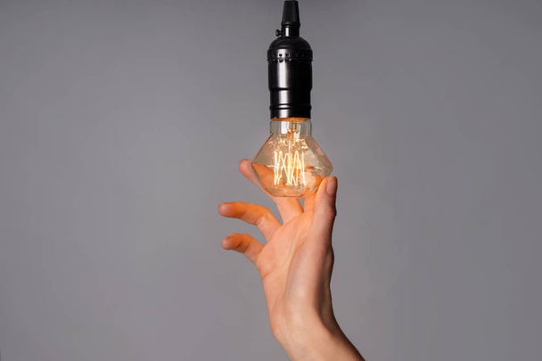 Female hand with glowing light bulb on grey background - Fotoğraf, Görsel
