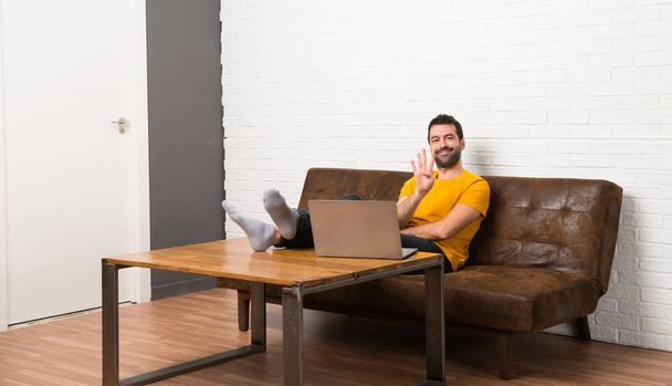 Чоловік з ноутбуком в кімнаті щасливий і рахуючи чотири пальцями
 - Фото, зображення