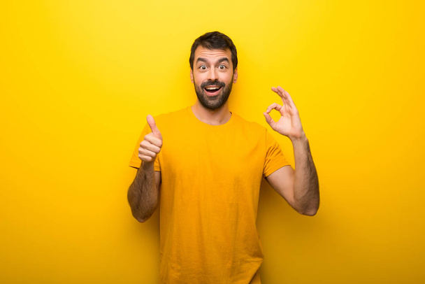 Человек на изолированных ярко-желтый цвет показывая OK знак и давая большой палец вверх жест
 - Фото, изображение