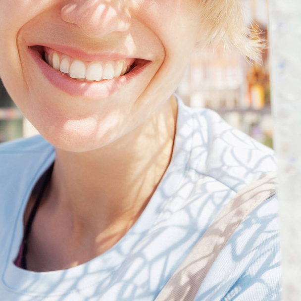 Lachende vrouw met gladde gezonde glimlach op zonnige straat close-up. Zomer positieve anoniem portret - Foto, afbeelding